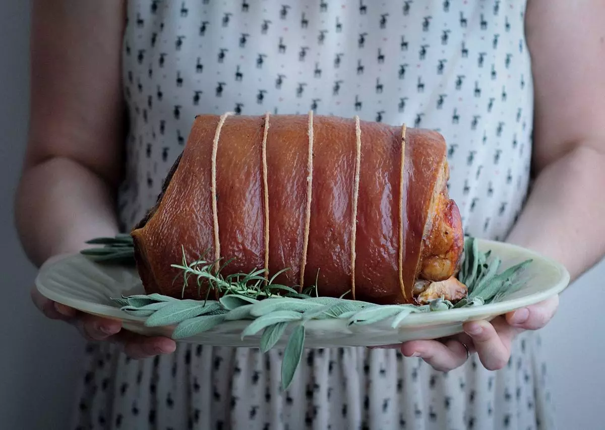Pessoa segurando prato com porchetta assada e ervas frescas