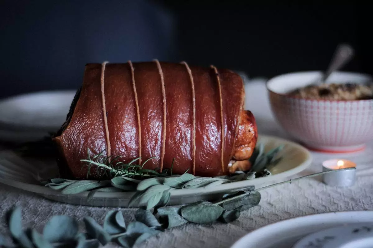 Porchetta assada com ervas, amarrada com barbante, sobre tábua de madeira